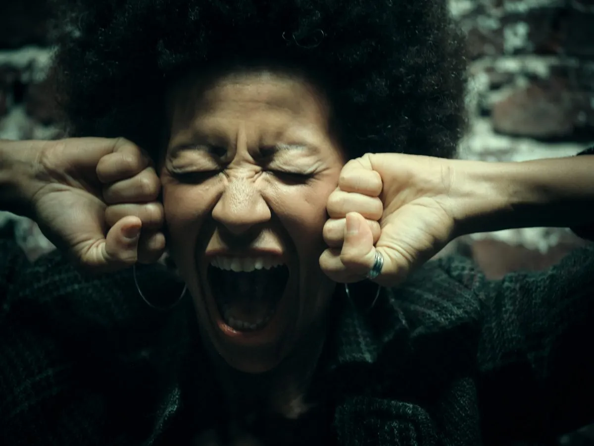 Close-up of a woman with afro hairstyle yelling with intense emotion against a brickwall.